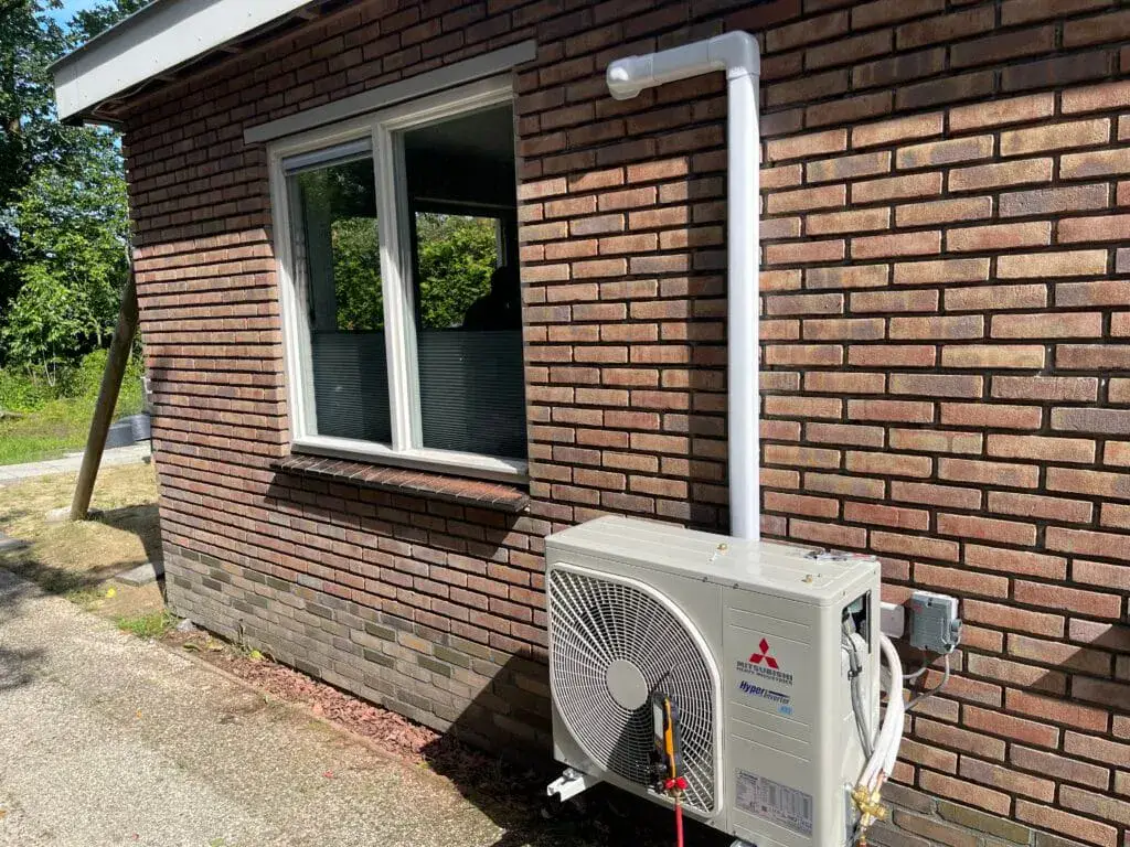 Buitenunit aan de gevel met de leiding in een witte goot, in Een